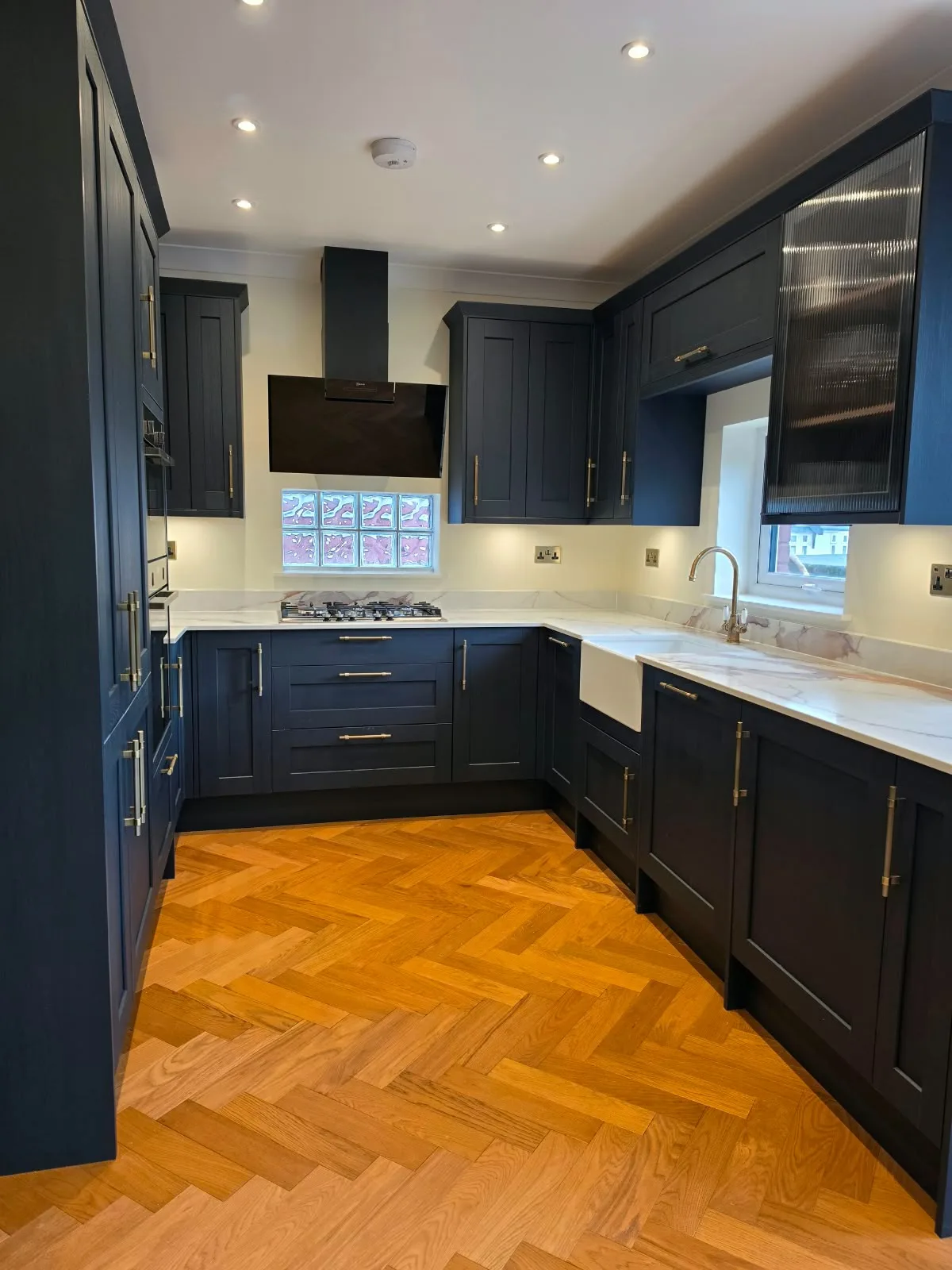 Modern kitchen renovation with dark blue cabinetry, white countertops, and herringbone wooden floor