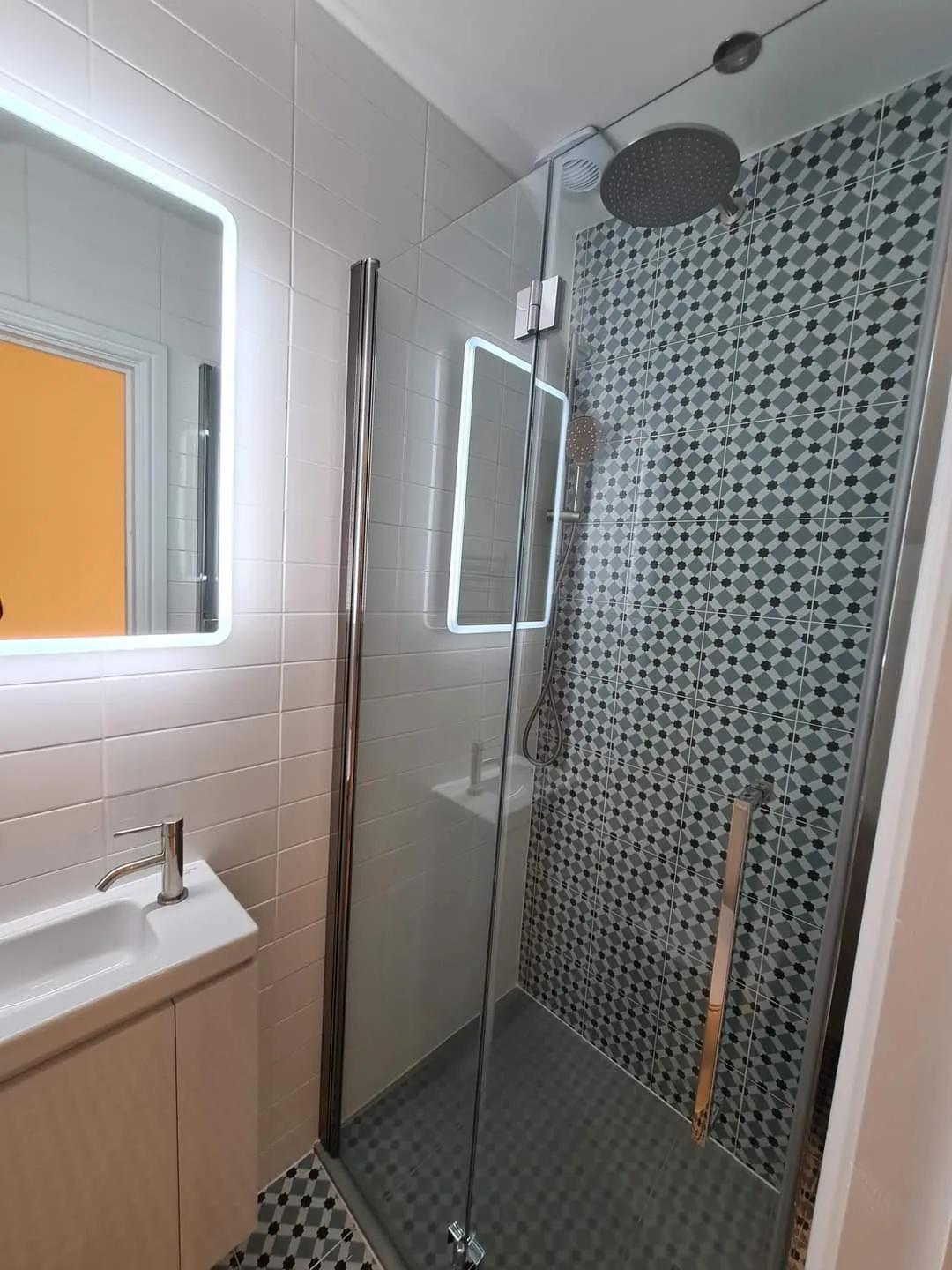 Modern bathroom with a glass shower, decorative tiles, and a stylish mirror