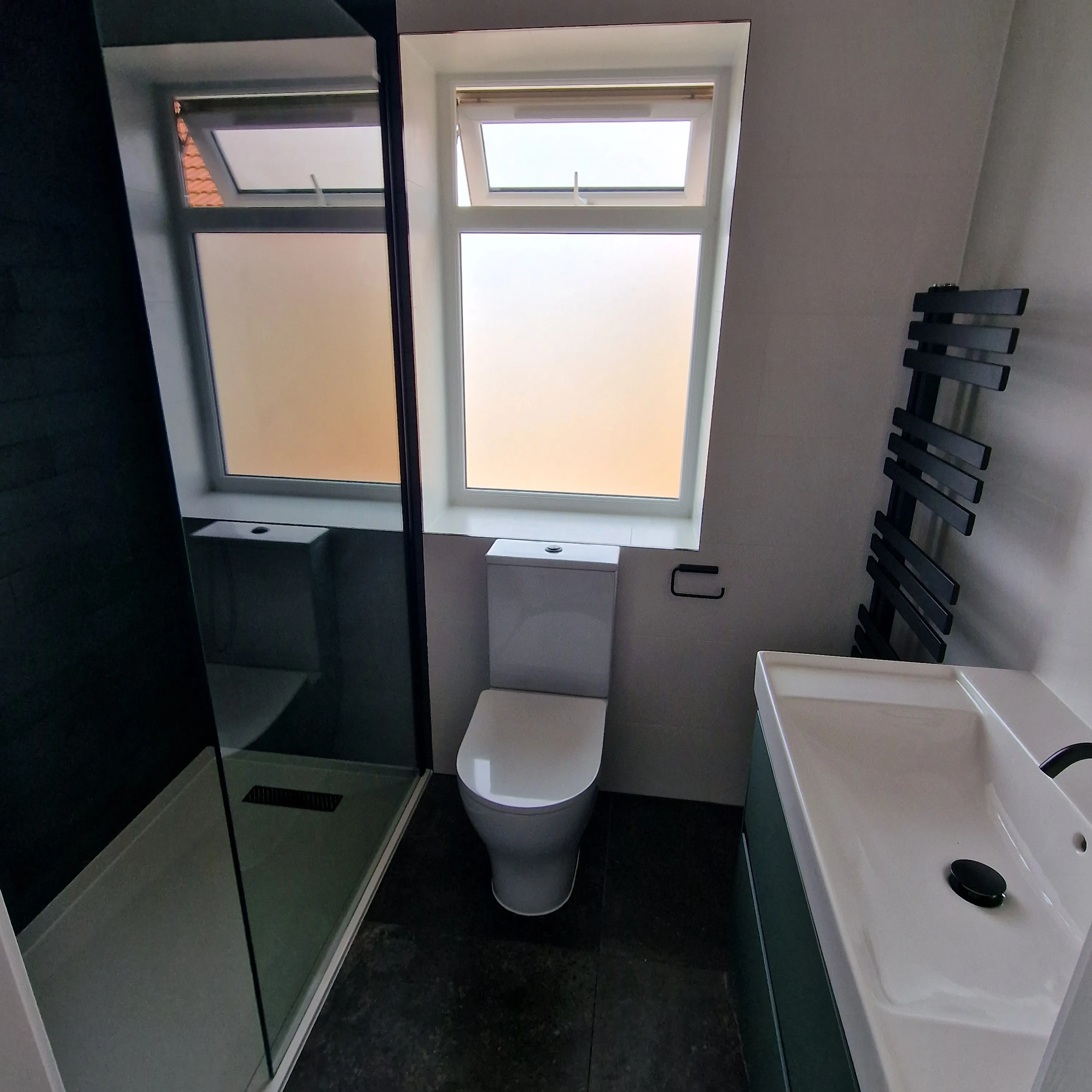 Modern bathroom with a shower, toilet, and sink, featuring sleek design and natural light
