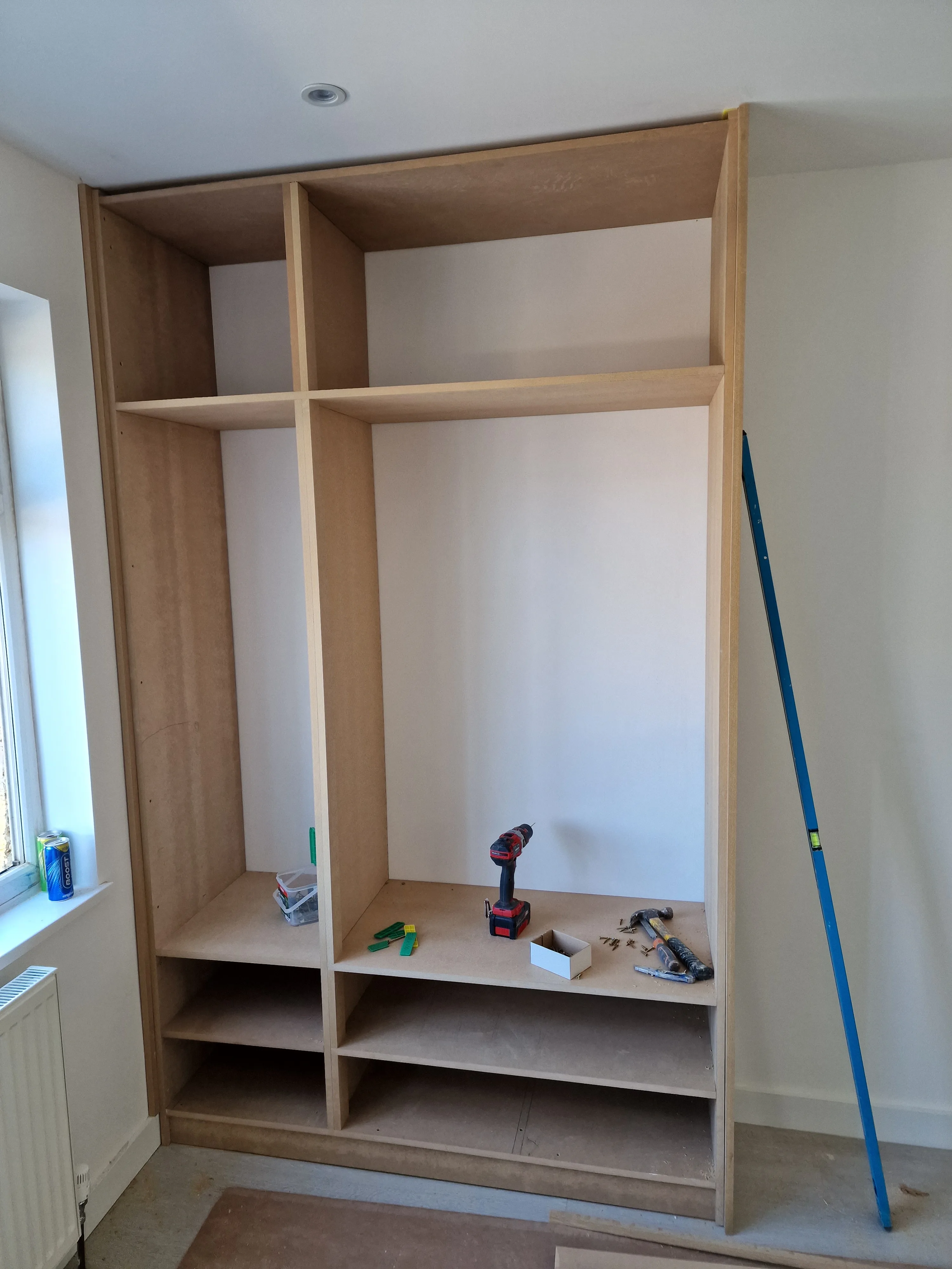 Custom wooden wardrobe installation in a bright room, showing open shelving and tools