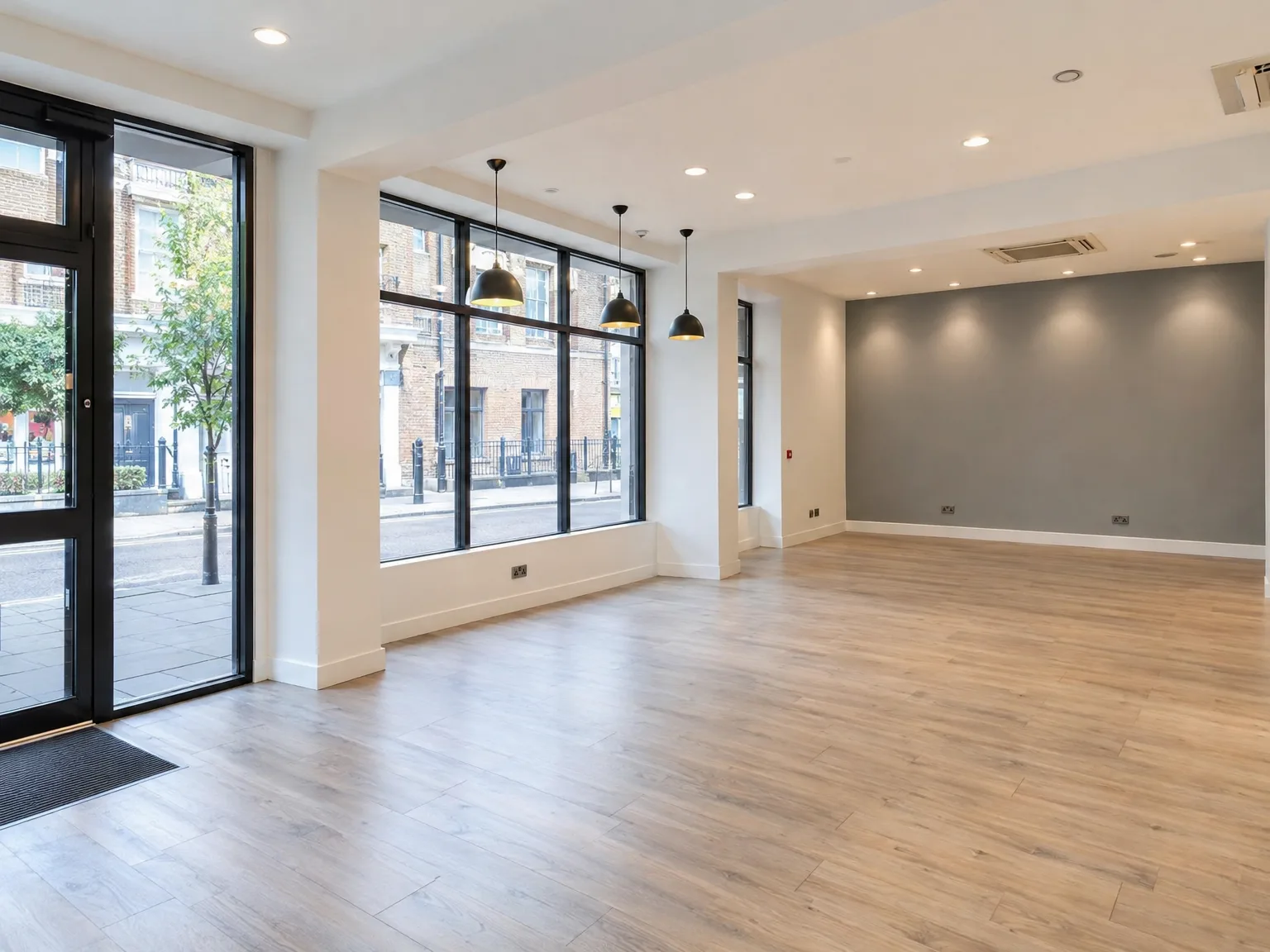 Modern commercial interior: wooden flooring with white walls, black-framed storefront windows, and pendant lighting