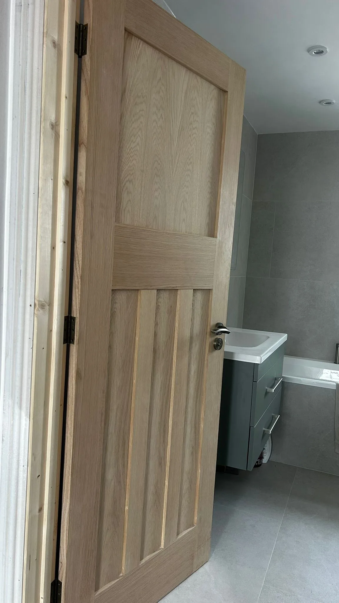 Modern wooden door in a bathroom renovation with grey tiles and vanity