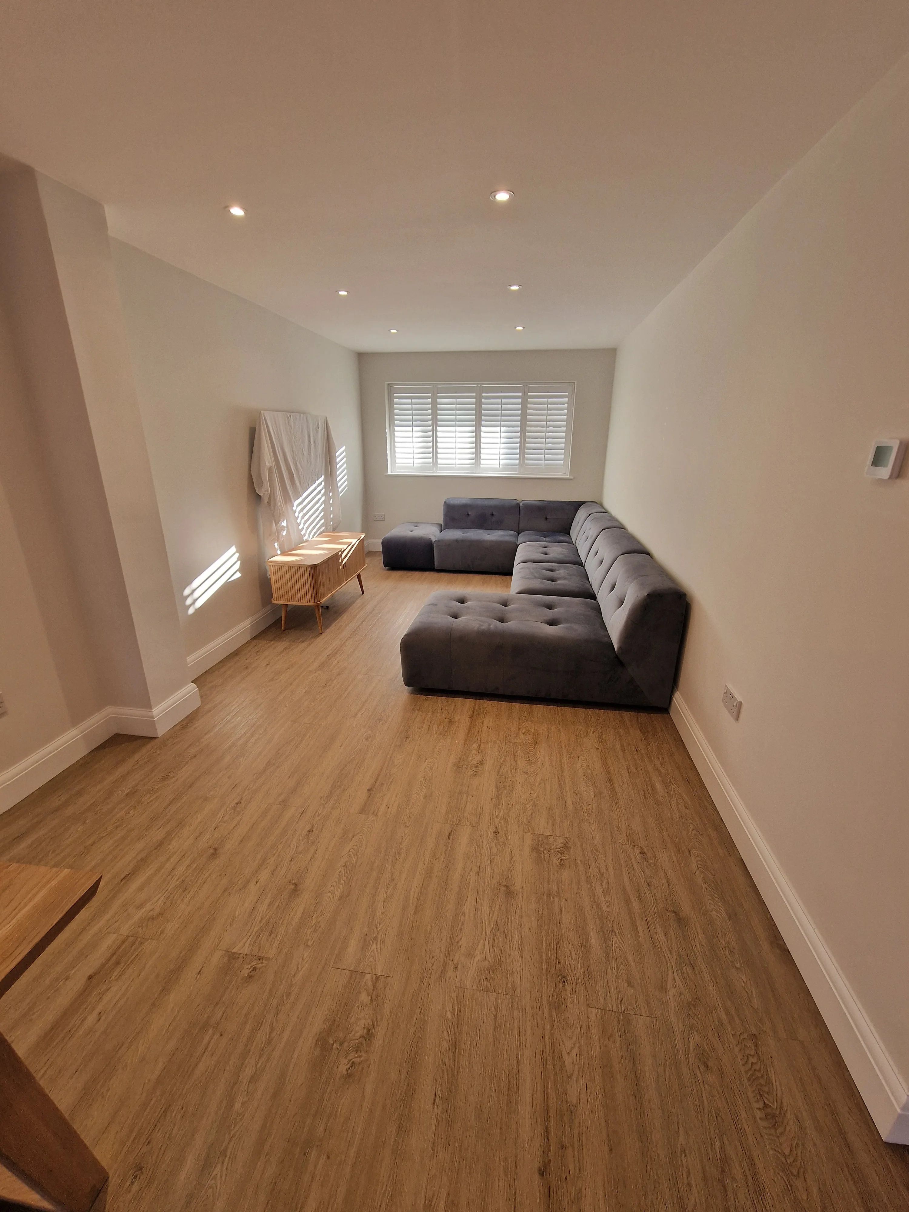 Modern living room with a grey sectional sofa and wooden flooring, showcasing home refurbishment