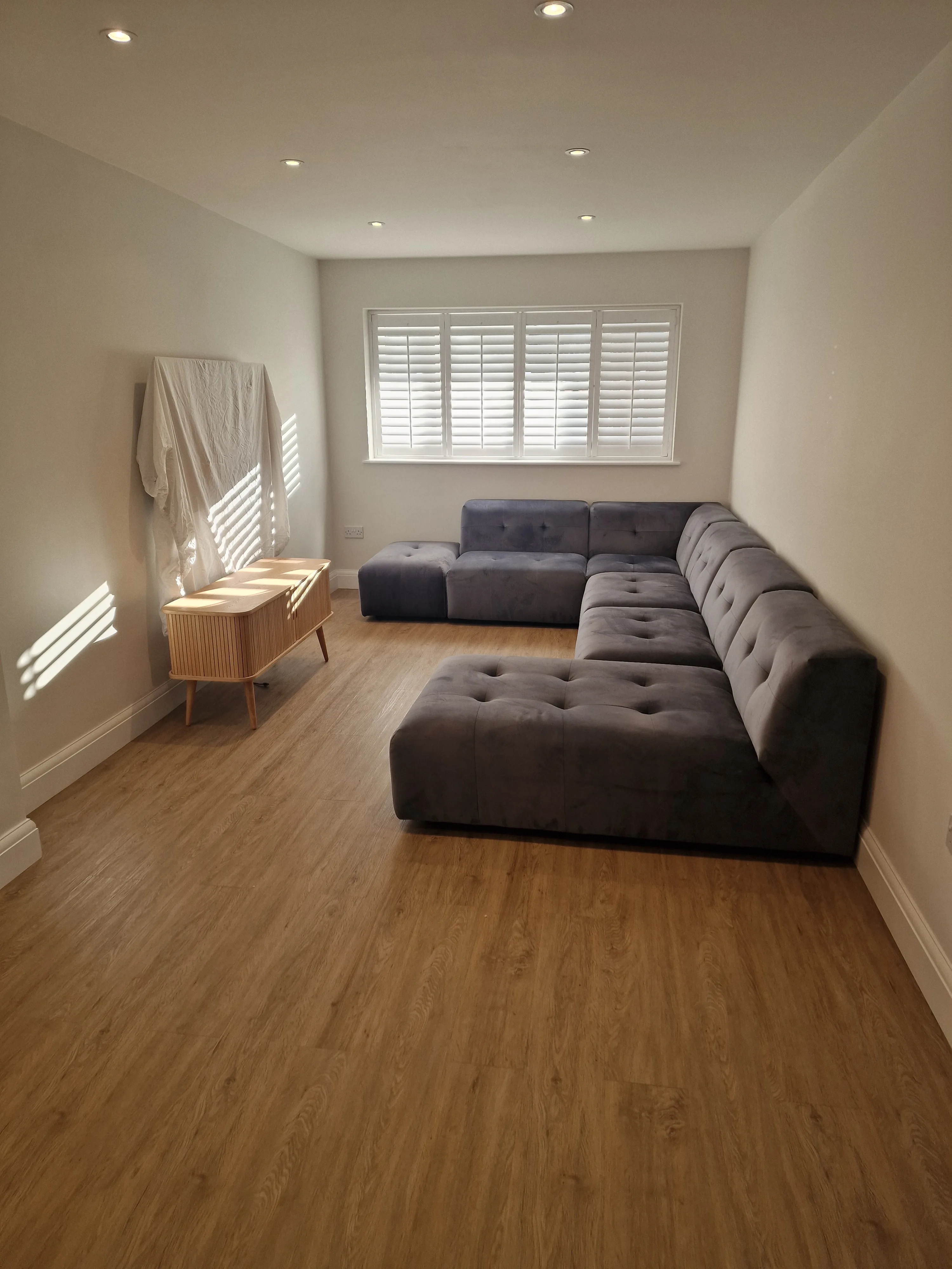 Modern living room with a large gray sectional sofa and natural light from window shutters