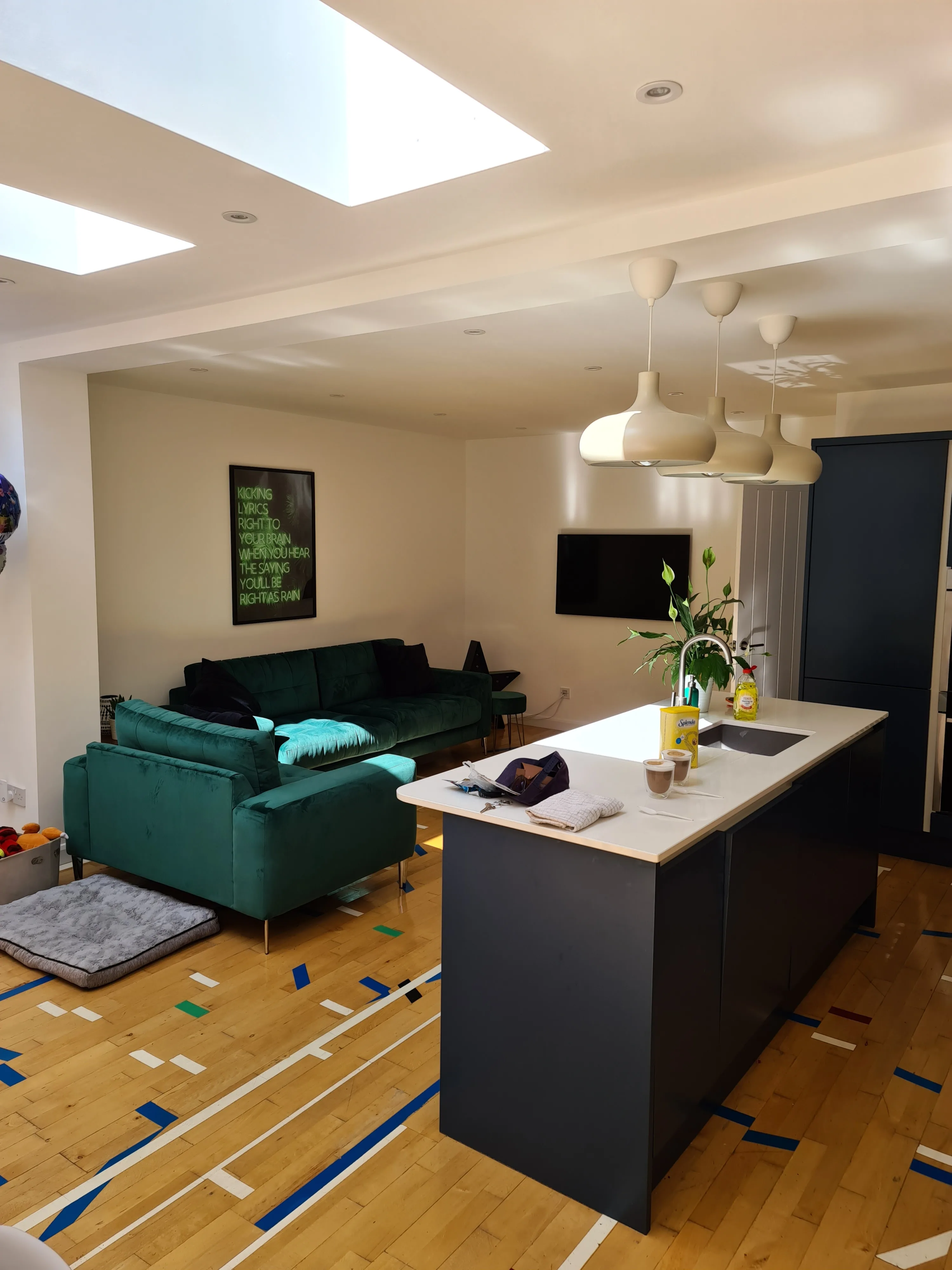 Modern kitchen and living area with a green sofa, island bar, and natural light from skylights