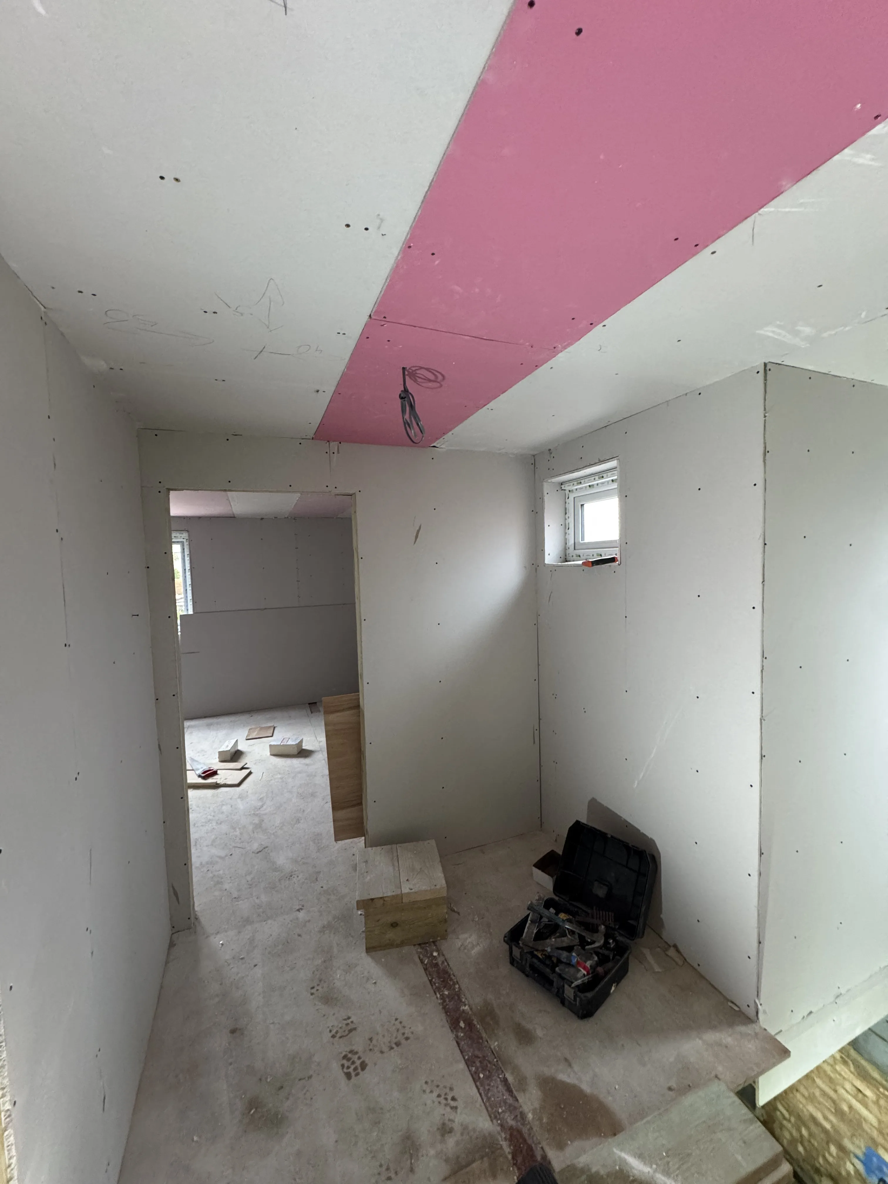 Interior view of a room under renovation, showcasing drywall installation and tools