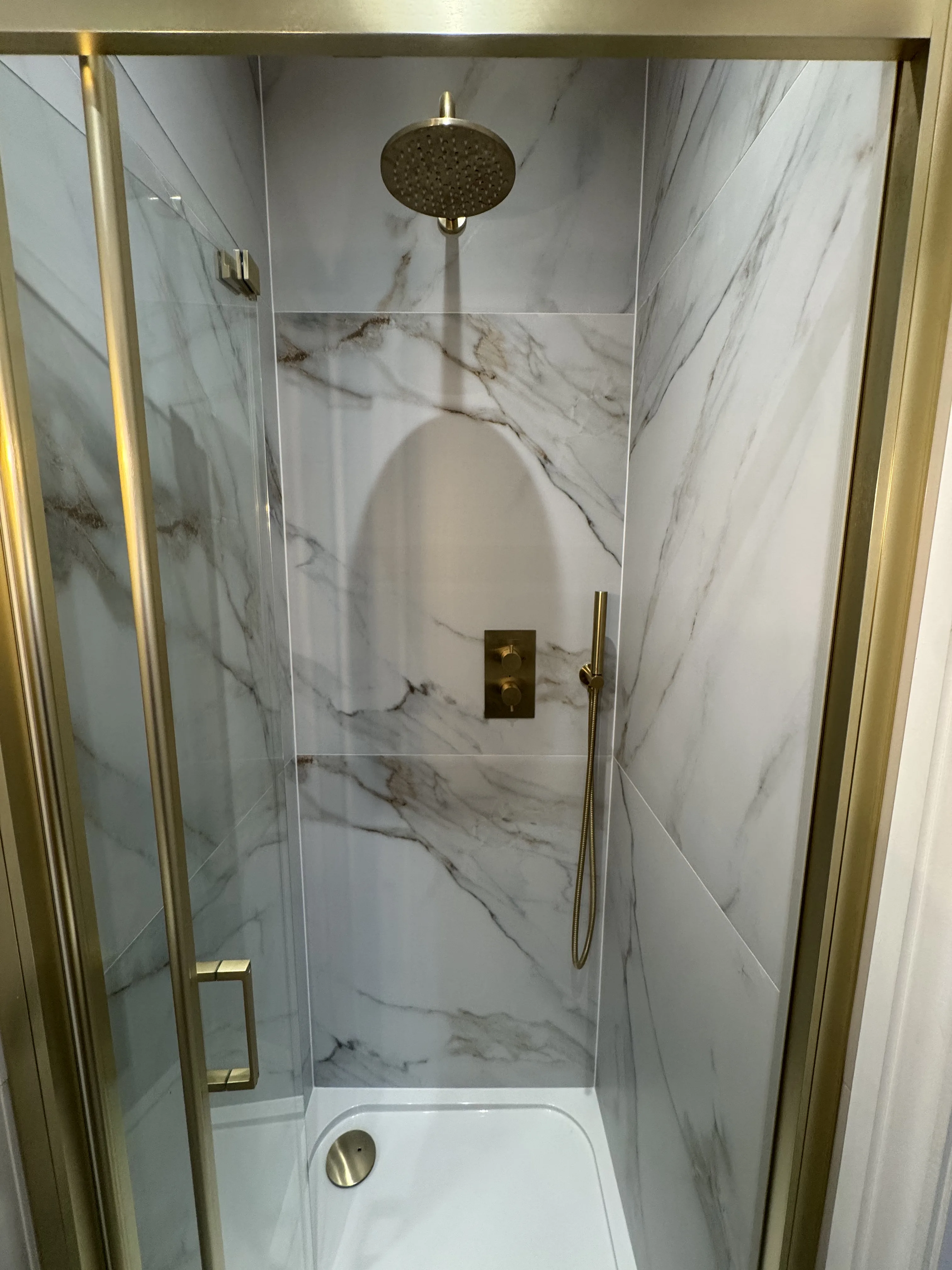 Modern bathroom shower renovation with marble tiles and gold fixtures