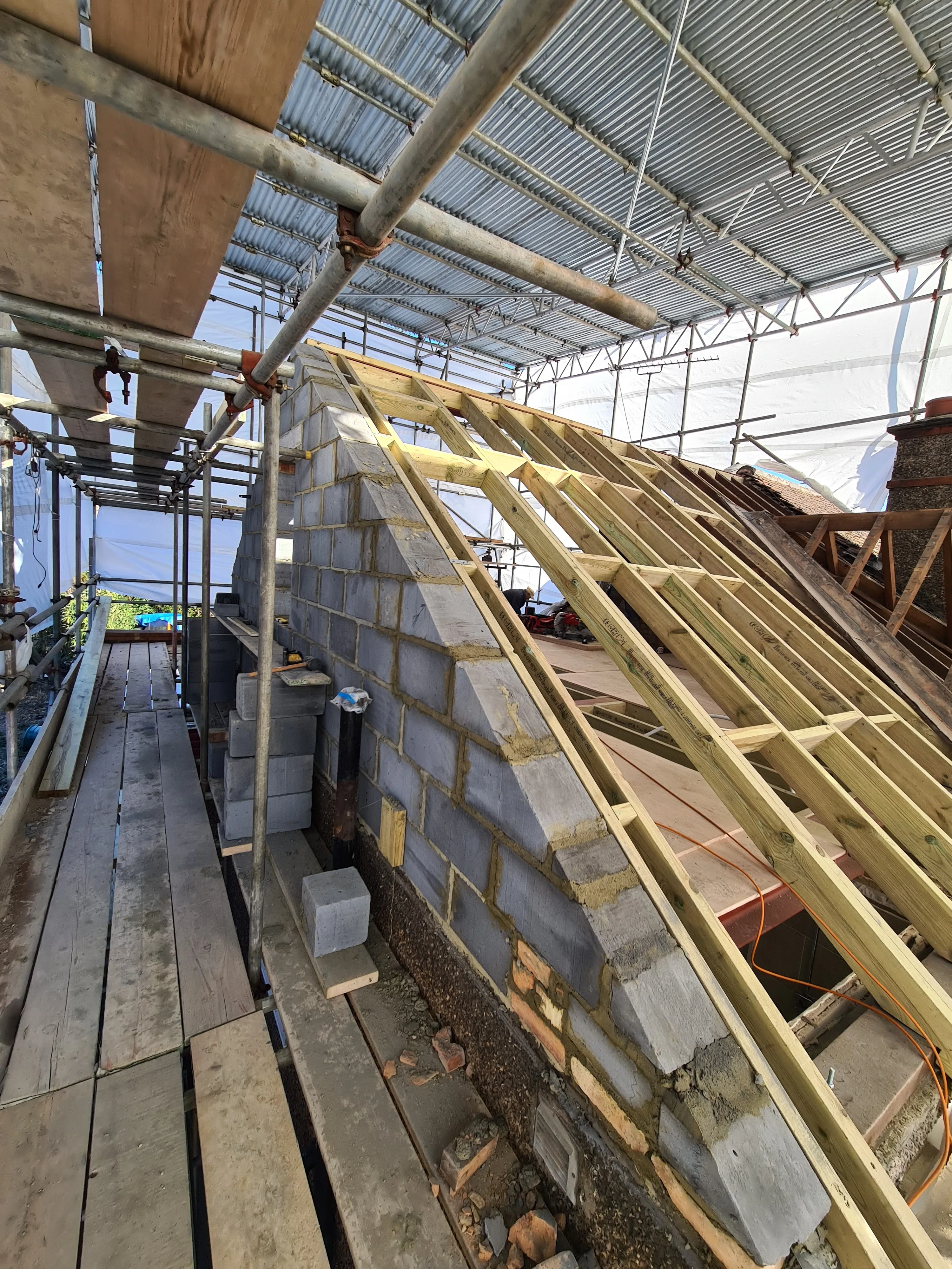 Construction site showing roof framing with scaffolding in the background, indicating renovation work