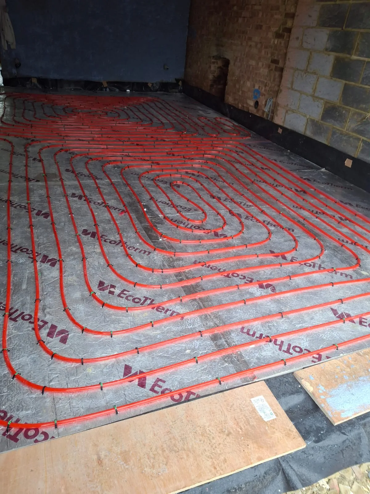 Underfloor heating system installation with red piping laid on a concrete floor