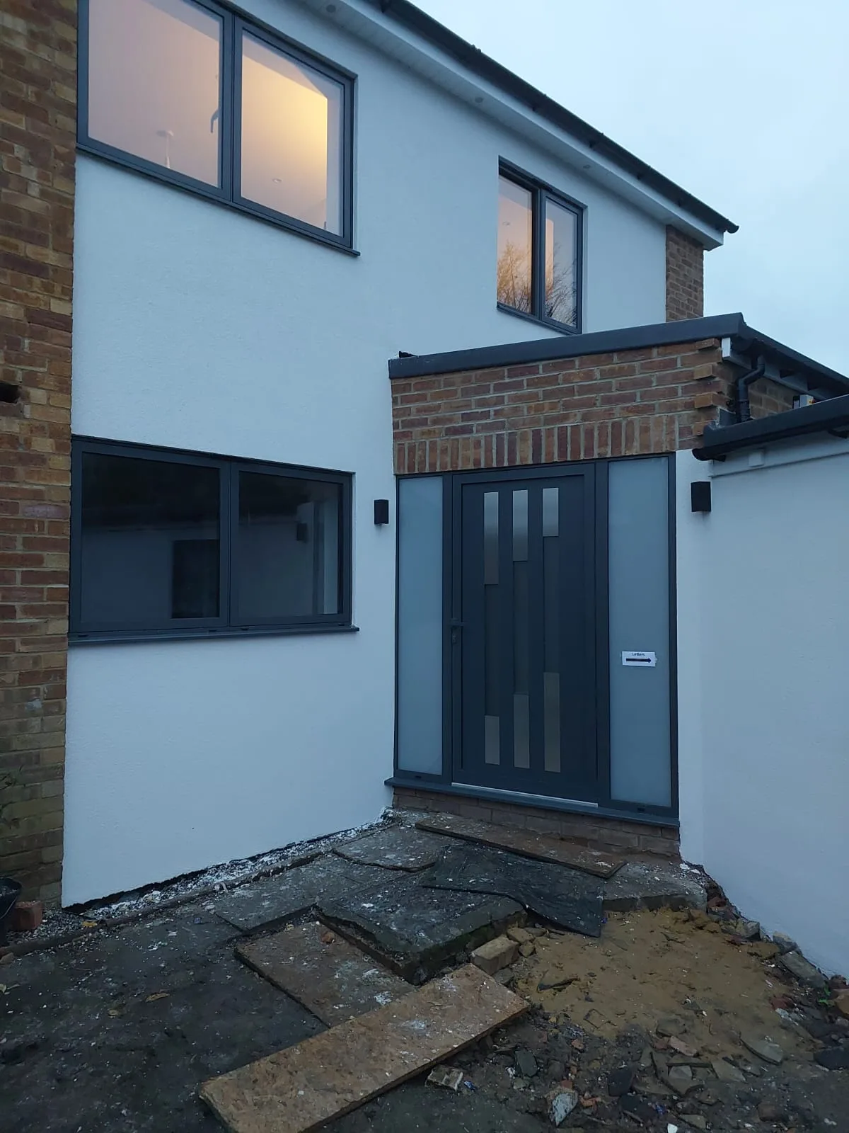 Modern entrance with a grey door and large windows, showcasing house renovation
