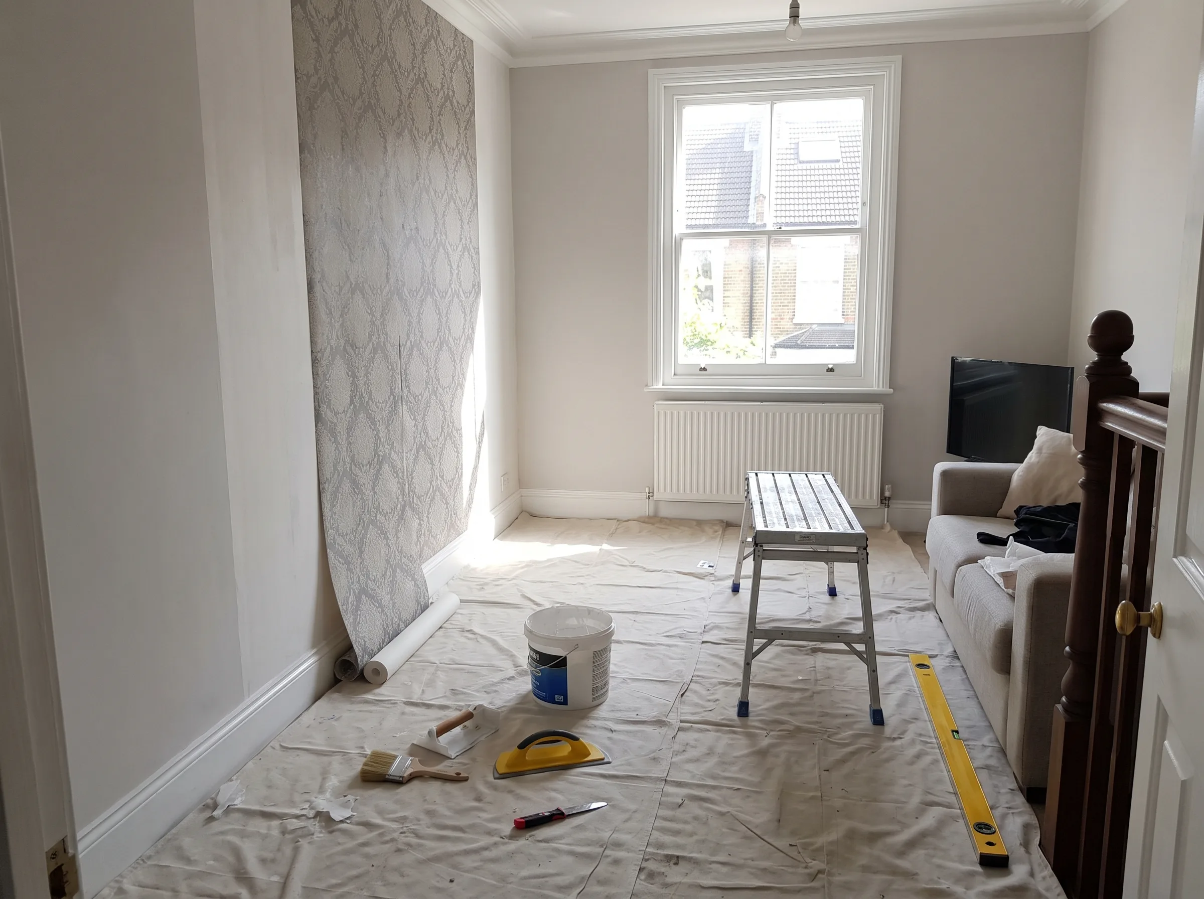Living room undergoing refurbishment with wallpaper, paint, and tools present