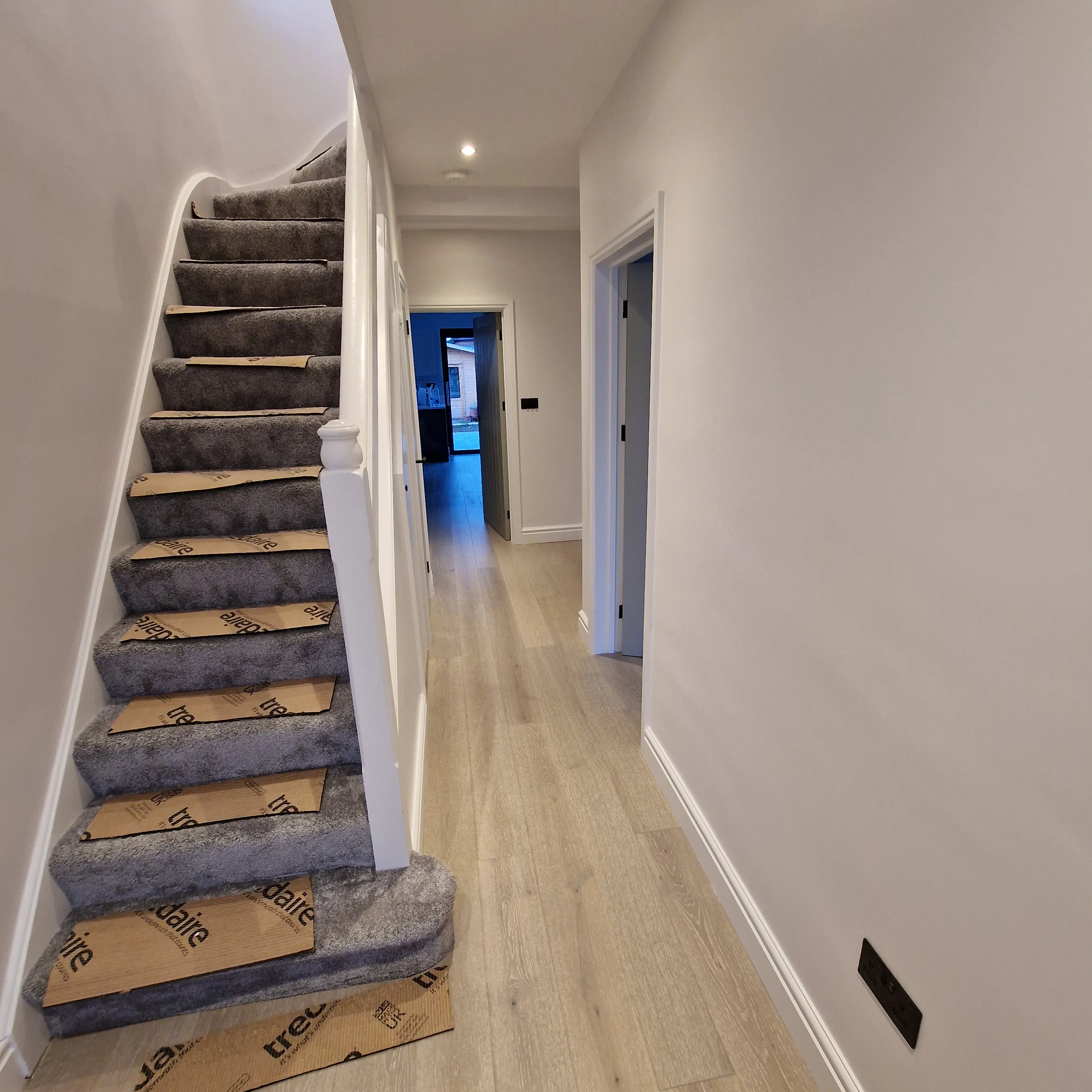Modern hallway featuring a carpeted staircase and wooden flooring