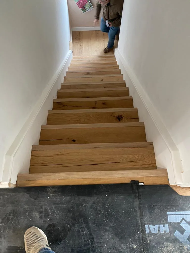 View of wooden stairs leading down with a person walking in the background, showcasing carpentry work